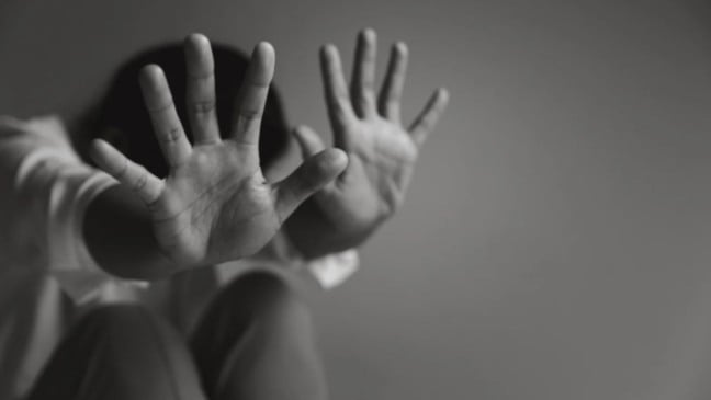 Pessoa com as mãos erguidas em sinal de defesa, representando vulnerabilidade e tentativa de proteção diante de violência.