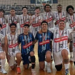 Atletas do vôlei masculino sub-21 de Jundiaí posam em quadra, usando uniformes branco e azul, mostrando medalhas de bronze ao lado do técnico.