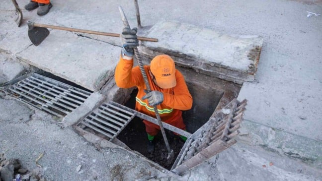 Funcionário da Prefeitura de Jundiaí faz limpeza de boca de lobo durante ação da Operação contra Enchentes.