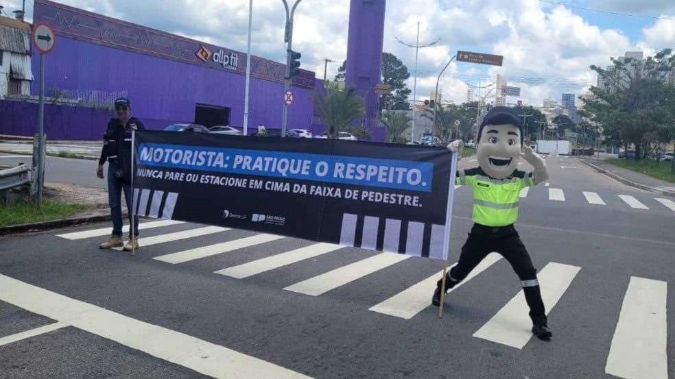 Agentes de trânsito e mascote Vaguinho seguram faixa educativa sobre respeito à faixa de pedestres durante ação em rua de Jundiaí. Agentes de trânsito e mascote Vaguinho seguram faixa educativa sobre respeito à faixa de pedestres durante ação em rua de Jundiaí.