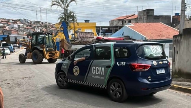 Viatura da GCM de Várzea Paulista acompanha ação integrada da Prefeitura na Vila Popular, com máquina realizando serviços urbanos em rua do bairro.