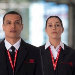 Dois vigilantes do Grupo GR, um homem e uma mulher, usando uniforme social com crach&aacute; da empresa, em ambiente corporativo.