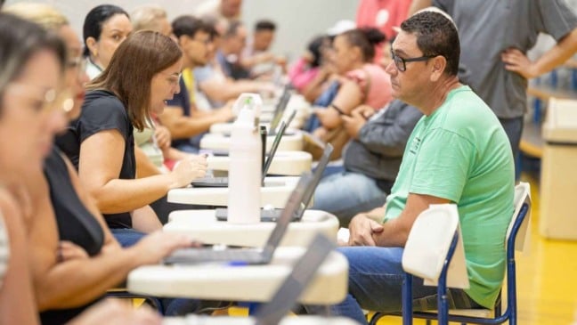 Moradores são atendidos individualmente por equipes da Prefeitura durante plantão de inscrições habitacionais, com uso de notebooks em um ginásio de Jundiaí.