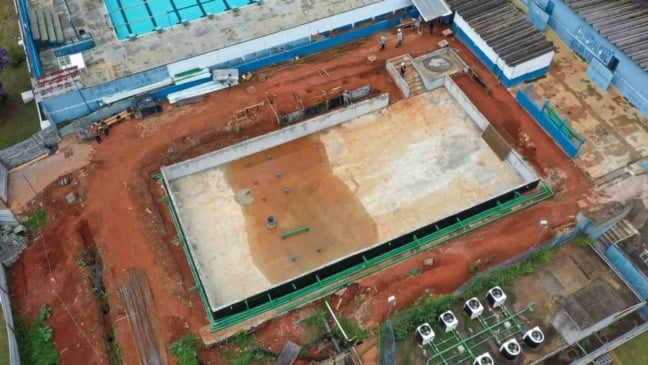 Imagem aérea das obras da piscina semiolímpica do Bolão, em Jundiaí, com tanque em construção, tubulações e área do complexo esportivo ao redor.