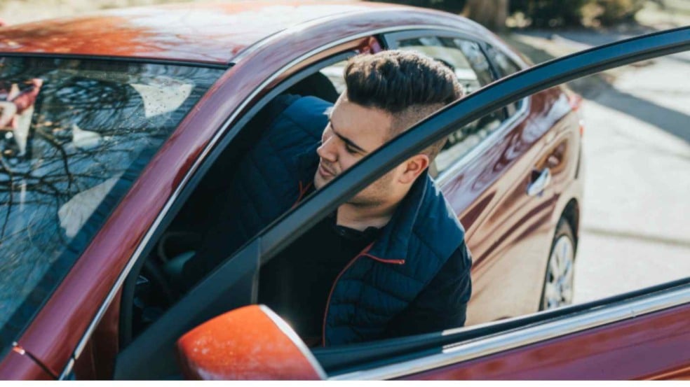 Motorista em carro vermelho com a porta aberta, observando o trânsito em uma rua arborizada durante o dia. Motorista em carro vermelho com a porta aberta, observando o trânsito em uma rua arborizada durante o dia.