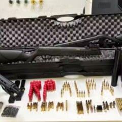 Armas de fogo, muni&ccedil;&otilde;es e carregadores apreendidos pela pol&iacute;cia est&atilde;o organizados sobre uma mesa, incluindo carabinas, pistola, cartuchos e estojos de transporte.