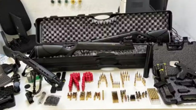 Armas de fogo, munições e carregadores apreendidos pela polícia estão organizados sobre uma mesa, incluindo carabinas, pistola, cartuchos e estojos de transporte.