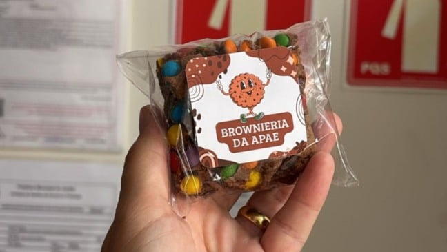 Brownie embalado da Brownieria da APAE, com rótulo ilustrado e pedaços de chocolate coloridos, segurado por uma mão.