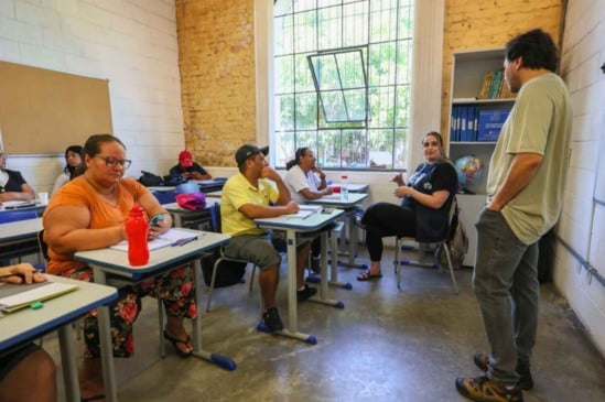 Alunos adultos participam de aula no Centro Municipal de Educação de Jovens e Adultos (CMEJA), em Jundiaí, com professor em sala de aula.