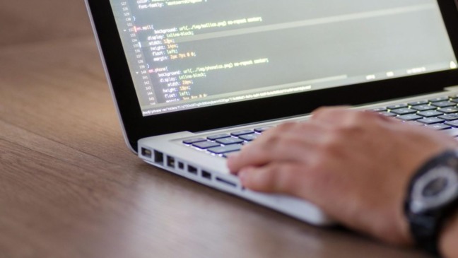 Pessoa digitando em notebook com código na tela, simbolizando cursos e qualificação profissional.