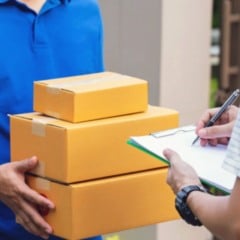 Entregador com caixas de encomendas realiza entrega enquanto cliente assina comprovante de recebimento.