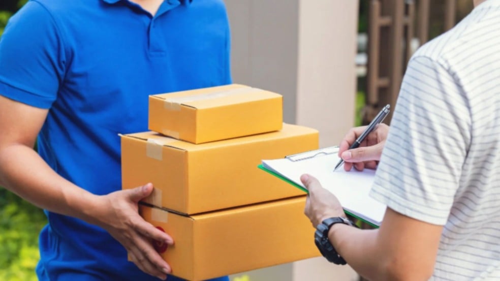 Entregador com caixas de encomendas realiza entrega enquanto cliente assina comprovante de recebimento. Entregador com caixas de encomendas realiza entrega enquanto cliente assina comprovante de recebimento.