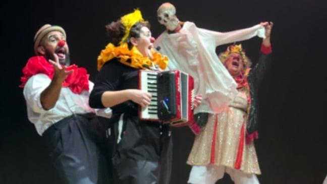 Artistas caracterizados como palhaços se apresentam em espetáculo circense com música ao vivo, figurinos coloridos e clima festivo.
