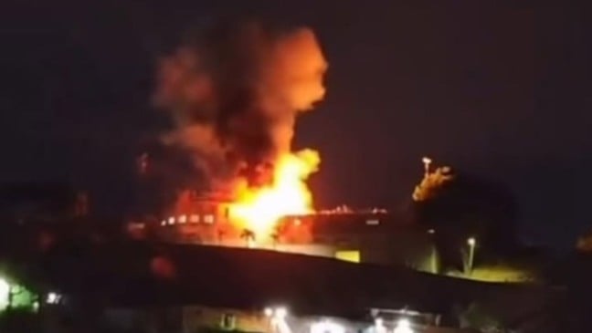 Explosão de grandes proporções ilumina prédio durante a noite, com chamas intensas e fumaça densa subindo ao céu em área urbana da Venezuela.