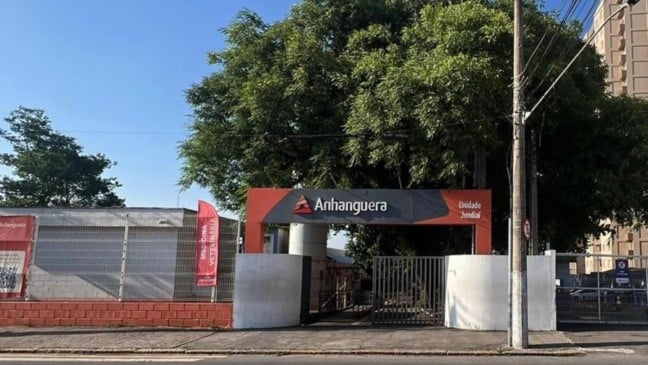 Fachada da Faculdade Anhanguera de Jundiaí, com portão de entrada, placa identificando a unidade e árvores ao redor, em dia ensolarado.