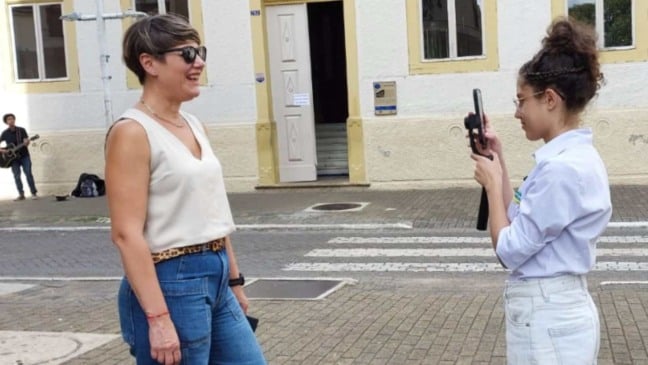 Mulher é gravada por jovem com celular em frente a prédio histórico no Centro de Jundiaí, com fachada antiga e músico de rua ao fundo.