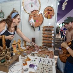 Artes&atilde; apresenta acess&oacute;rios e objetos artesanais em estande da Festa da Uva, enquanto visitantes observam e escolhem produtos feitos com materiais naturais.