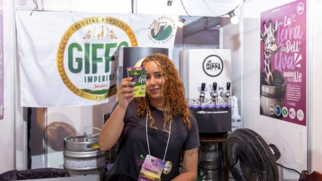 Expositora da Giffa Imperial Cervejaria segura copo de cerveja artesanal no estande da marca durante a Festa da Uva de Jundiaí.