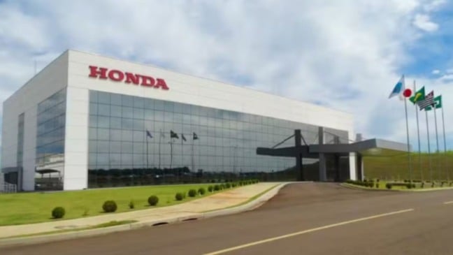 Fachada do prédio da Honda Brasil com arquitetura moderna, fachada de vidro, logotipo da marca em destaque e bandeiras hasteadas na entrada.