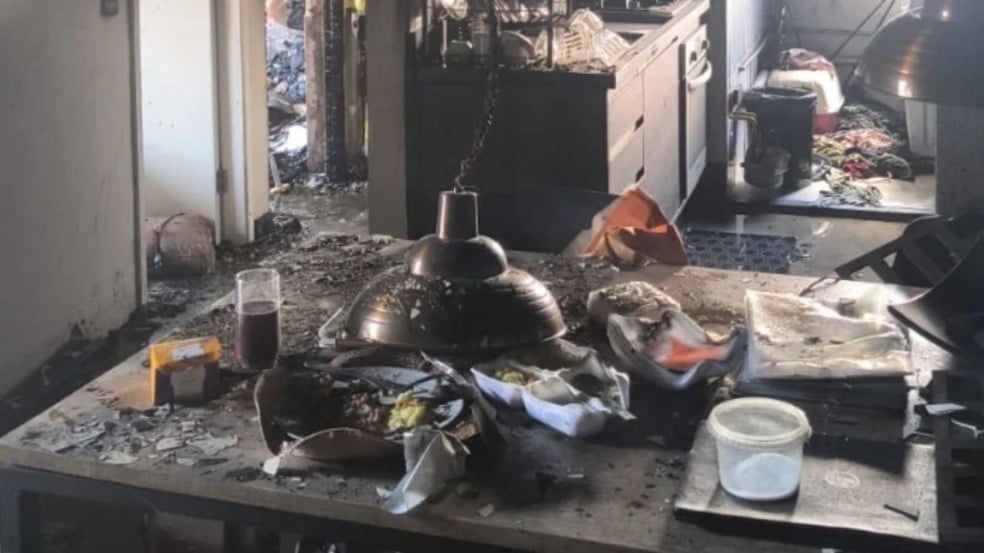 Interior de apartamento destruído por incêndio, com mesa coberta de objetos queimados, fuligem e utensílios derretidos. Interior de apartamento destruído por incêndio, com mesa coberta de objetos queimados, fuligem e utensílios derretidos.