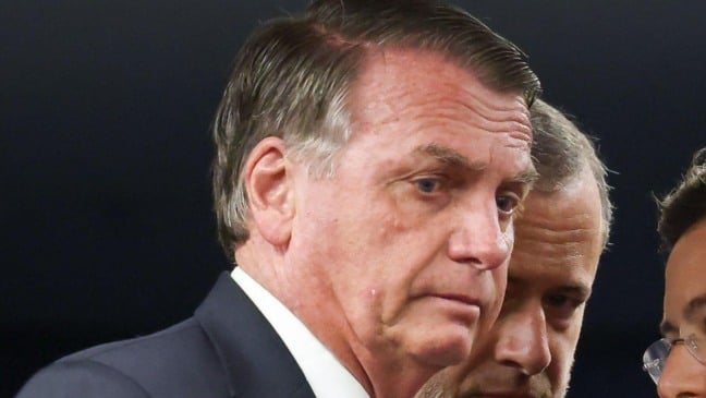 Jair Bolsonaro com expressão séria ao lado de assessores