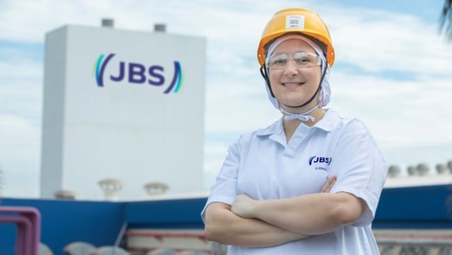 Funcionária da indústria de alimentos usa capacete e uniforme de segurança em frente a unidade industrial da JBS no interior de São Paulo.