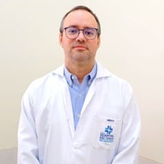 Dr. Marco Aur&eacute;lio, m&eacute;dico infectologista, posa para foto usando jaleco do Hospital S&atilde;o Vicente em ambiente interno e neutro.