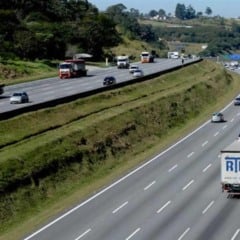 Rodovia do Sistema Anhanguera-Bandeirantes com tr&aacute;fego intenso de caminh&otilde;es e carros, pistas duplicadas e canteiro central verde.