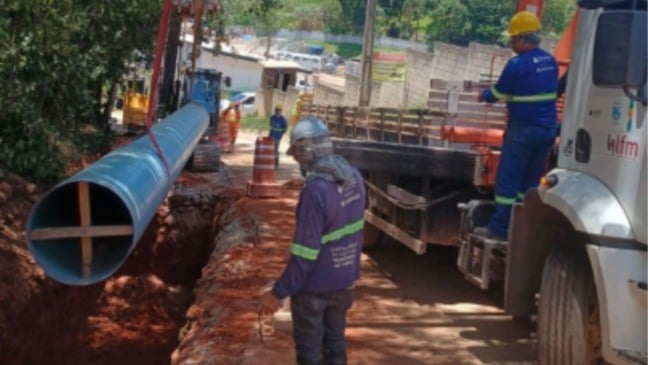 Trabalhadores instalam adutora de grande porte em obra de ampliação do sistema de abastecimento de água, com uso de caminhão e equipamentos de segurança.