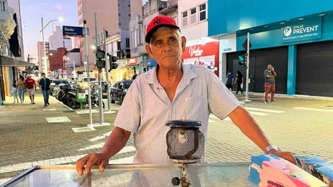 Pipoqueiro Isaías em seu carrinho de pipoca no Centro de Jundiaí, à noite, com comércio e pedestres ao fundo.