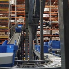 Interior de centro de distribui&ccedil;&atilde;o com esteiras autom&aacute;ticas, caixas azuis e prateleiras industriais usadas na opera&ccedil;&atilde;o log&iacute;stica.