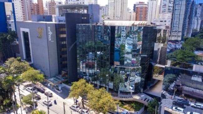 Vista aérea de hospital da Rede D’Or em São Paulo, com fachada de vidro espelhado, prédios ao redor e ruas movimentadas.