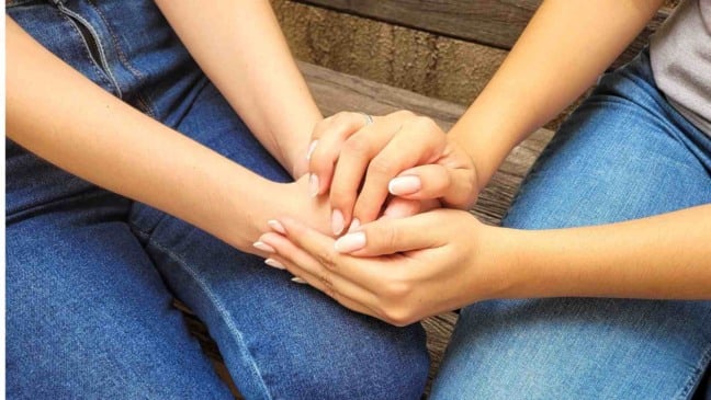 Duas pessoas sentadas seguram as mãos em gesto de apoio e acolhimento, simbolizando cuidado emocional e saúde mental.