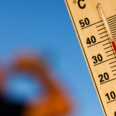 Term&ocirc;metro marcando alta temperatura, perto de 40 &deg;C, com pessoa desfocada ao fundo reagindo ao calor sob c&eacute;u azul.