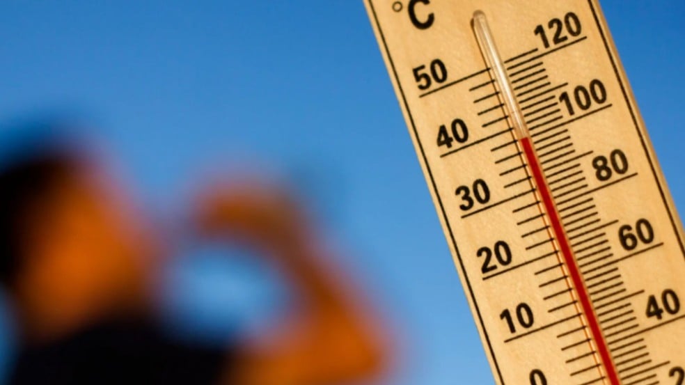 Termômetro marcando alta temperatura, perto de 40 °C, com pessoa desfocada ao fundo reagindo ao calor sob céu azul. Termômetro marcando alta temperatura, perto de 40 °C, com pessoa desfocada ao fundo reagindo ao calor sob céu azul.
