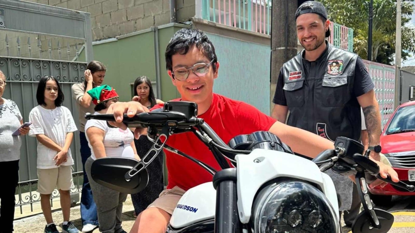 Jovem com s&iacute;ndrome de Down participa de atividade externa e sorri ao sentar em motocicleta durante a&ccedil;&atilde;o inclusiva da Teia Down.