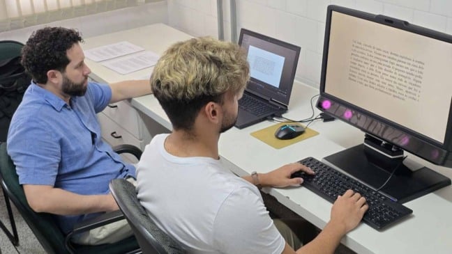 Participante realiza teste de rastreamento ocular em computador, enquanto pesquisador acompanha o experimento em laboratório da Faculdade de Medicina de Jundiaí.