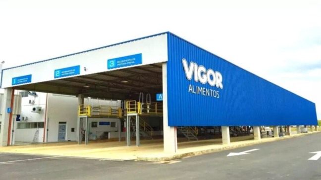 Fachada da unidade industrial da Vigor Alimentos, com prédio azul e branco e logotipo da empresa em destaque.