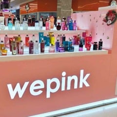 Quiosque da Wepink em shopping, com perfumes e cosm&eacute;ticos expostos em prateleiras iluminadas e logotipo da marca em destaque.