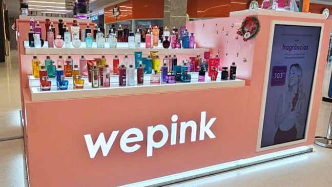 Quiosque da Wepink em shopping, com perfumes e cosméticos expostos em prateleiras iluminadas e logotipo da marca em destaque.