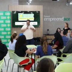 Empres&aacute;rios participam de rodada de neg&oacute;cios da ACE Jundia&iacute; em sala de eventos, enquanto palestrante fala ao p&uacute;blico com microfone.