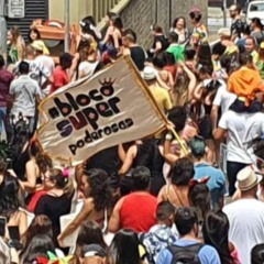 Foli&otilde;es acompanham o desfile do Bloco Super Poderosas no Centro de Jundia&iacute;, com estandarte do bloco erguido entre o p&uacute;blico durante o Carnaval de rua.