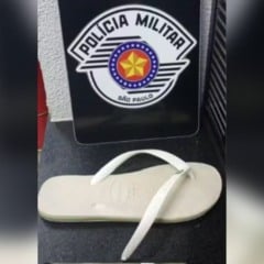 Chinelo branco com tira quebrada apreendido pela Pol&iacute;cia Militar de S&atilde;o Paulo, exibido em frente ao bras&atilde;o da corpora&ccedil;&atilde;o.