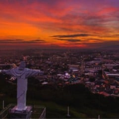 Est&aacute;tua do Cristo de Itupeva vista do alto ao p&ocirc;r do sol, com a cidade ao fundo e c&eacute;u em tons alaranjados e avermelhados.