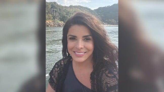 Mara Maravilha sorri para a câmera em foto ao ar livre, com rio e morros cobertos por vegetação ao fundo.