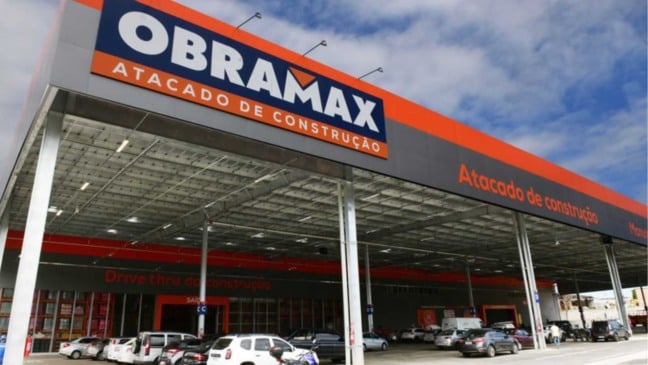 Fachada da Obramax em São Paulo, atacarejo de materiais de construção, com letreiro da marca e estacionamento com veículos.