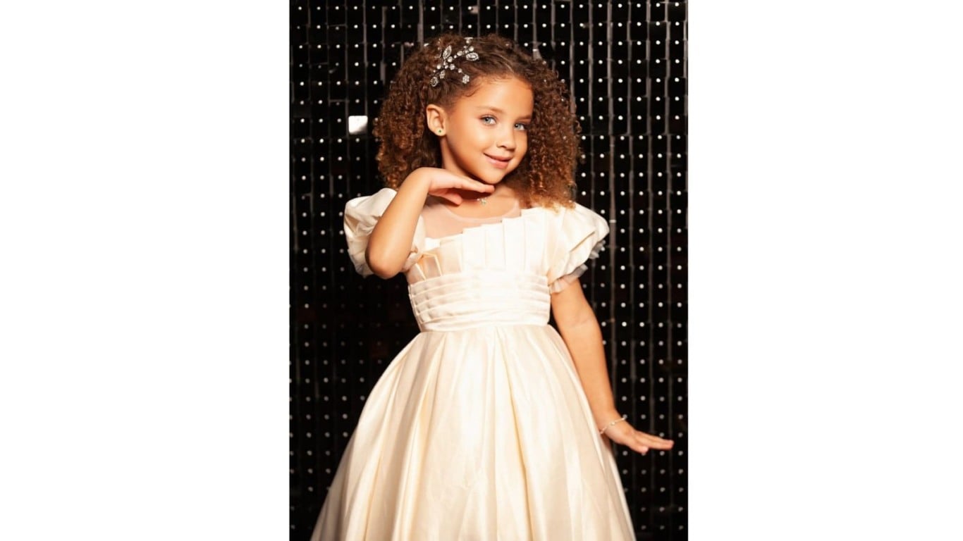 Pietra posa com vestido de gala claro e fundo iluminado.