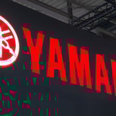 Logotipo do Grupo Yamaha Brasil iluminado em vermelho sobre fundo escuro, exibido em ambiente interno corporativo.