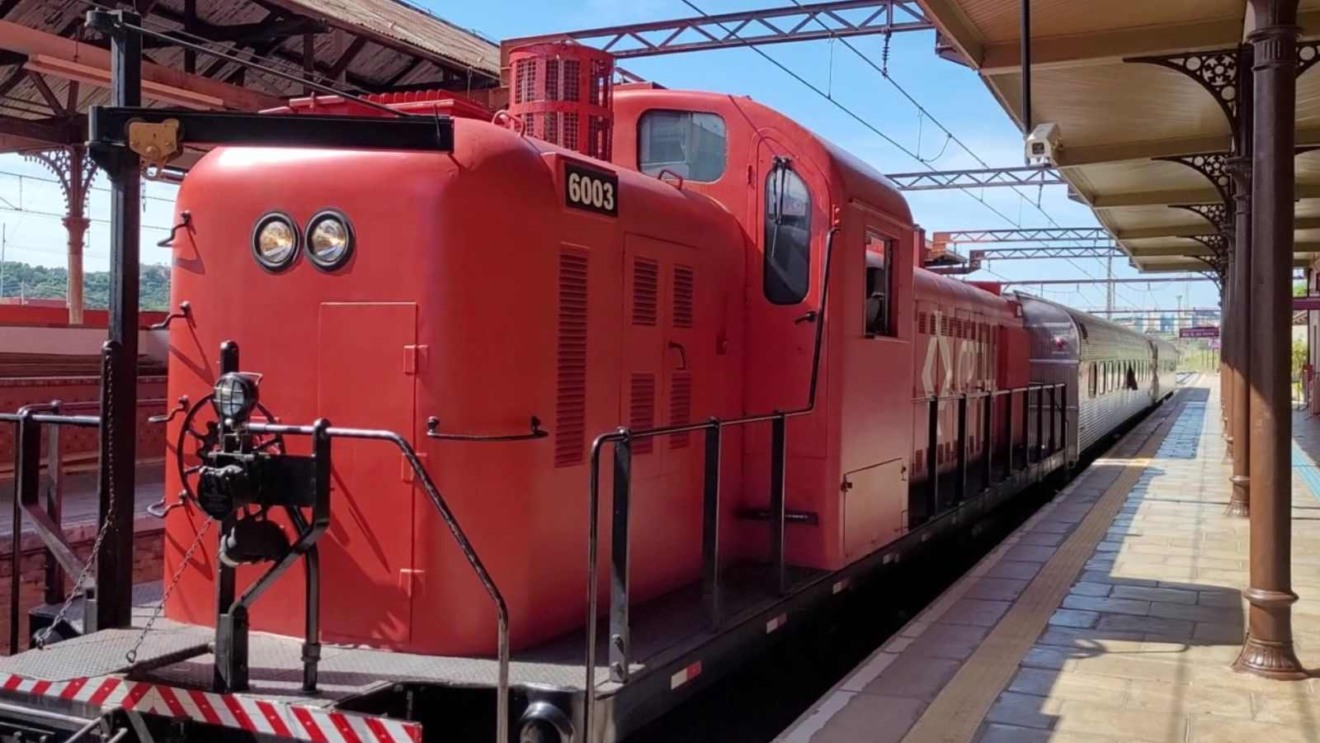 Locomotiva vermelha do Expresso Turístico da CPTM parada na estação com vagões de passageiros ao fundo.